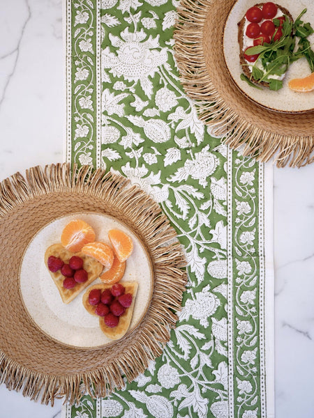 Two woven placemats with plates of food on a decorative table runner.