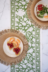 Two woven placemats with plates of food on a decorative table runner.