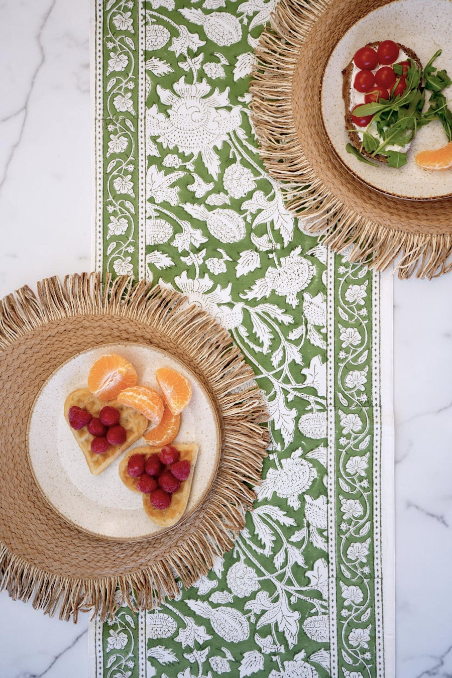 Two woven placemats with plates of food on a decorative table runner.